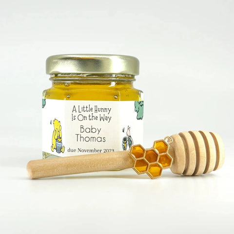 2 oz jar of honey with gold lid, 3" wooden honey dipper, enamel honeycomb charm, and personalized Winnie the Pooh label with A Little Hunny Is On the Way title.