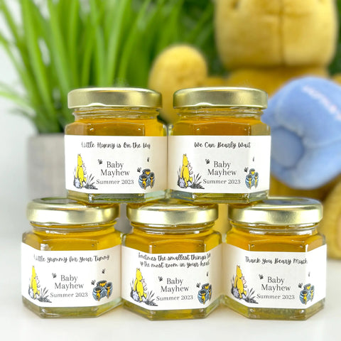 2 oz honey baby shower party favors with gold lids and personalized Winnie the Pooh labels. Labels show Winnie the Pooh and his honey pots. Titles shown include A Little Hunny is On the Way, We Can Bearly Wait, A Little Yummy for Your Tummt, Thank You Beary Much, and Sometimes the smallest things take up the most room in your heart.