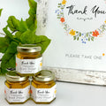 2 oz honey thank you wedding party shower favors on hexagon jars with gold lid with personalized labels. Labels feature wildflower design with Thank You title. Free matching printable table sign in background.