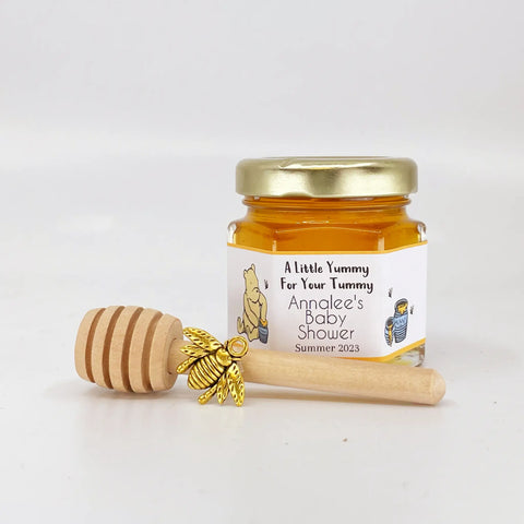 2 oz hexagon jar filled with honey, gold lid, gold bee charm, 3" wooden honey dipper and personalized Winnie the Pooh label design with hunny pots and yellow stripes and title that says A Little Yummy For Your Tummy.