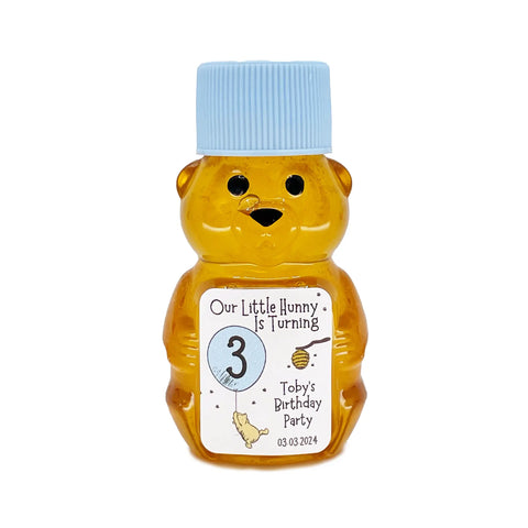 2 oz honey bear baby shower favor with baby blue cap and personalized label. Label shows classic Winnie the Pooh with a blue balloon with the title Our Little Hunny is Turning 3.