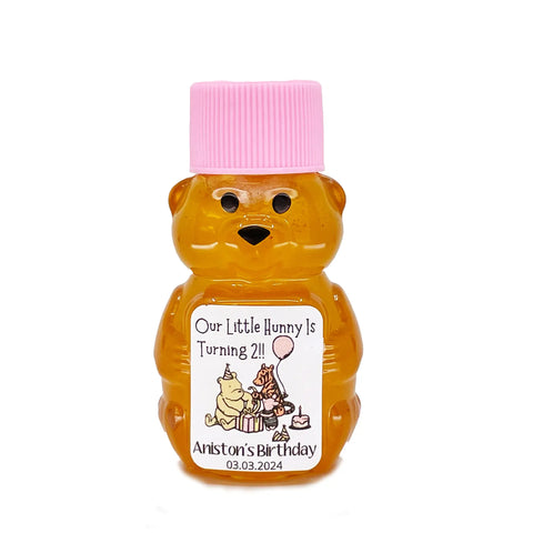 2 oz Winnie the Pooh honey bear baby shower favor with pink cap and personalized label. Label shows classic Winnie the Pooh, Piglet, and Tigger with pink party decorations with the title Our Little Hunny is Turning 2.