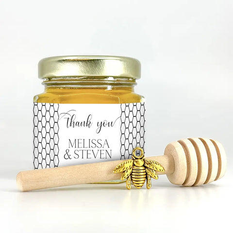 2 oz hexagon honey favor filled with honey. Jar has gold lid, 3" wooden honey dipper, gold bee charm, and personalized black and white honeycomb design on label with title Thank You.