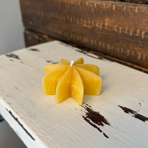 Yellow candle shaped like a flower on a rustic wooden surface