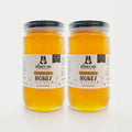 Two 3-lb jars of golden clover blossom honey with black lids and The Honey Jar branded labels. Labels say The Honey Jar Delicious Pure Raw Honey Clover Blossom Honey Raw and unfiltered.