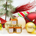 2 oz honey holiday Christmas party favor gift jars shown with gold lid and personalized holiday lights design on labels. Labels feature Bee Happy title. Christmas ornaments, lights, tree, and presents in background.