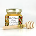 2 oz hexagon honey favor. Jar is filled with honey and has gold lid, 3" wooden honey dipper, gold bee charm, and personalized holiday lights label with title Bee Happy.