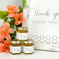 2 oz honey thank you wedding party shower favors on hexagon jars with gold lid and labels. Labels feature black and white honeycomb design with Thank You for Coming title. Free matching printable table sign in background.