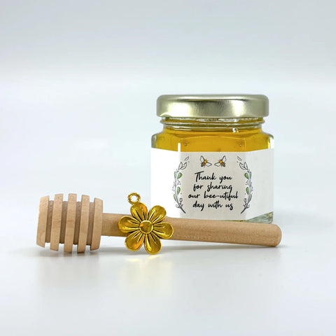 2 oz hexagon jar filled with honey, gold lid, 3" wooden honey dipper, gold flower charm, and rose laurel design on label with title Thank you for sharing our bee-utiful day with us.