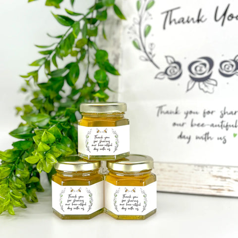 2 oz honey thank you wedding party shower favors on hexagon jars with gold lid and labels. Labels feature rose laurel design with title stating Thank you for sharing our bee-utiful day with us. Free matching printable table sign in background.