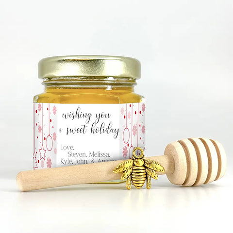 2 oz hexagon honey favor. Jar is filled with honey and has gold lid, 3" wooden honey dipper, gold bee charm, and personalized fine line ornament label with title wishing you a sweet holiday.