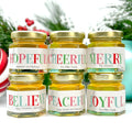 Close up of 2 oz honeyholiday Christmas party favor gift jars with gold lid and personalized labels. Labels feature multicolored holiday greeting  titles, including Bee Hopeful, Bee Cheerful, Bee Merry, Bee Joyful, Bee Peaceful, and Believe. Christmas decorations in background.