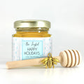 2 oz hexagon honey favor. Jar is filled with honey and has gold lid, 3" wooden honey dipper, gold bee charm, and personalized snowflake label with title Bee Joyful.