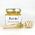 2 oz hexagon honey favor filled with honey. Jar has gold lid, 3" wooden honey dipper, gold bee charm, and personalized wildflower design on label with title Thank You.