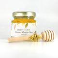 Honey favor single set shown. 2 oz hexagon jar filled with honey and topped with gold lid. Accessories shown include 3" wooden honey dipper, gold bee charm, and an autumn leaves label with title Bride to Bee.