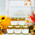 Stack of 2 oz honey favors with gold lids and fall trees labels in front of free matching printable sign. Titles on jars include Thank You, Meant to Bee, Fallen in Love, Bride to Bee, and Love is Sweet. Title shown on printable sign is Fallen in Love.