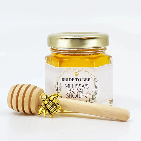 2 oz hexagon jar filled with honey, gold lid, 3" wooden honey dipper, gold bee charm, and personalized geometric design on label with title Bride to Bee.