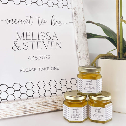 Wedding favor table shown with free printable sign and honey favor jars. Titles include meant to bee, bride to bee, bee our guest, love is sweet, thank you, and more. Contents include 2 oz hexagon jars filled with honey, gold lids, and personalized honeycomb-themed labels