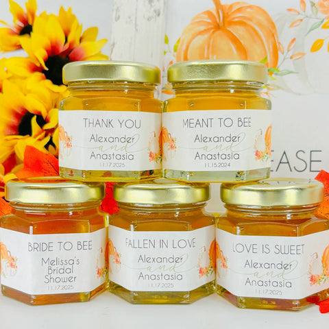 Close up of 2 oz honey wedding favors topped with gold lids. Labels on jars feature an autumn pumpkin design and different title options. Title options shown are Thank You, Meant to Bee, Bride to Bee, Fallen in Love, and Love is Sweet. 