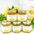 Close up of 2 oz hexagon honey wedding favors with gold lids and personalized sunflower bunch labels. Label titles include Love is Sweet, Meant to Bee, Bride to Bee, Thank You, and Found My Honey.