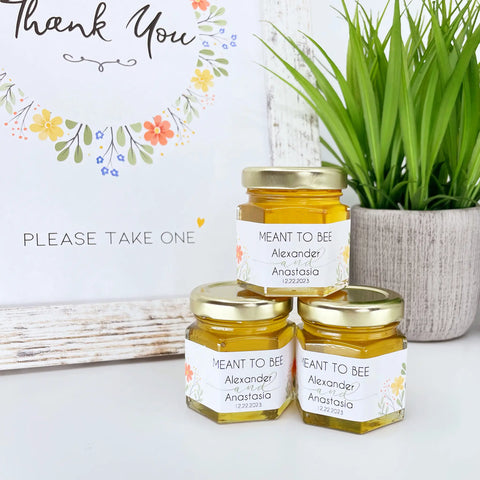 Wildflower theme honey wedding favors with personalized Meant to Bee label, and gold lid. Free printable sign is in the background with title Thank You.