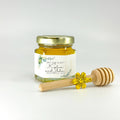 Example of honey favor set with accessories: 2 oz hexagon jar filled with honey, topped with gold lid, with personalized eucalyptus label. Accessories include 3" wooden honey dipper and gold flower charm. Label title shown is Bee Our Guest.