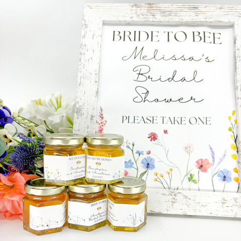 Honey wedding favors with free printable sign. Titles include Bee Our Guest, Bride to Bee, Found My Honey, Welcome, Love is Sweet, and more. Floral color options shown: red/pink, purple, yellow, blue, and multi. Contents include honey, 2 oz hexagon jar, gold lid, and personalized label.