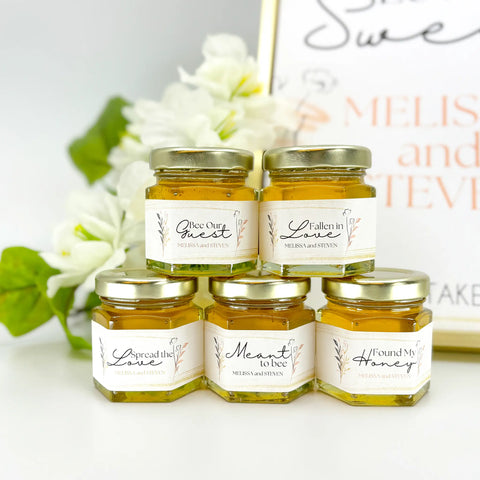 close up of rose gold floral wedding favors with personalized labels, honey, and gold lids. Title options include Bee Our Guest, Fallen in Love, Spread the Love, Meant to Bee, Found My Honey, and more.