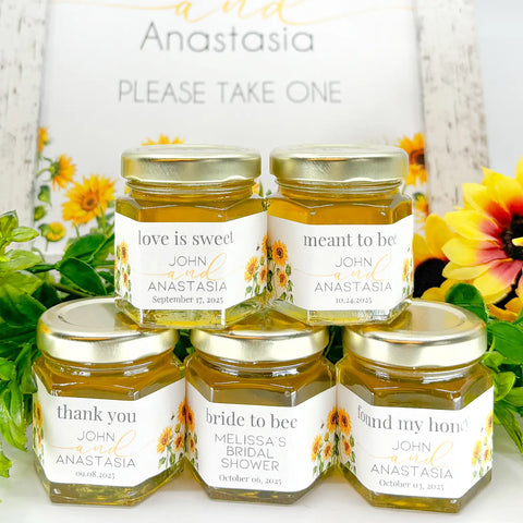 Close up of 2 oz hexagon honey wedding favors with gold lids and personalized sunflower field labels. Label titles include Love is Sweet, Meant to Bee, Bride to Bee, Thank You, and Found My Honey.